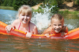 Happy little girls on mattress in lake