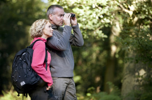 Mature couple standing in the countryside, man looking through binoculars