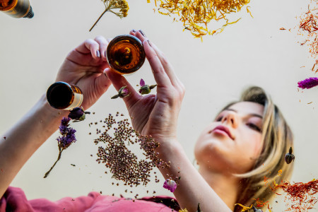 Young woman perfumer preparing herbs and flowers for make a perfume. Under table view.