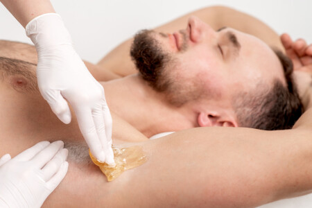 Cosmetologist applying wax paste on male armpit